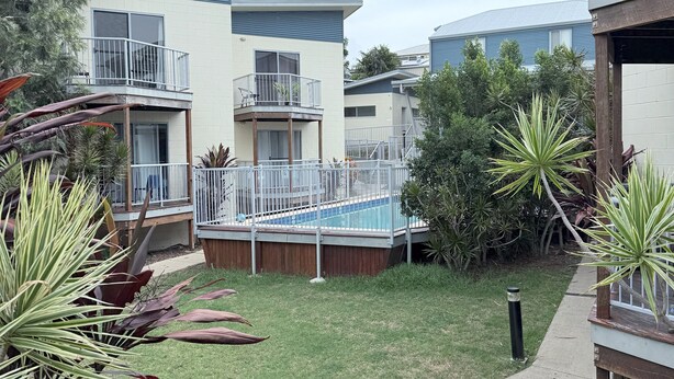 Un immeuble résidentiel doté d’une piscine, entouré de diverses plantes et d’une pelouse bien entretenue.