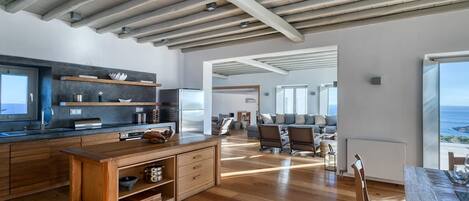 A spacious living area with a wooden dining table, a kitchen with modern appliances, and a view of the sea.