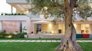 A modern house with a large tree in the front yard, a dining area with outdoor seating, and a well-maintained lawn. - Villa Bel Prato with pool - My Rental Homes (Modica)