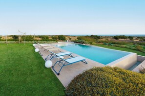A rectangular pool with a clear view of the horizon, surrounded by a well-maintained lawn and a row of sun loungers. - Villa Bel Prato with pool - My Rental Homes (Modica)