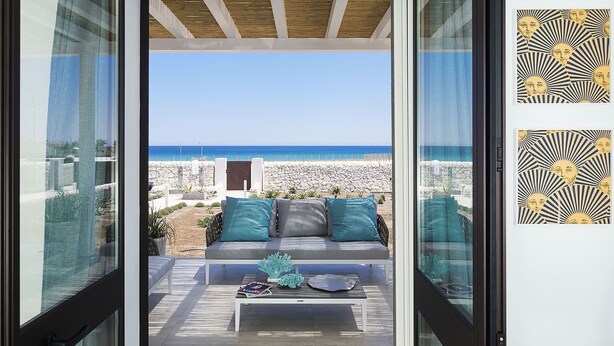 Una sala de estar moderna con vista a la playa, una pared de piedra y un techo de madera.