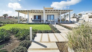 Una casa moderna con un porche cubierto, césped y un muro de piedra.
