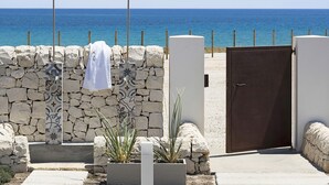 Un muro de piedra con una toalla colgada en un accesorio de metal, una puerta cerrada y vista al mar.