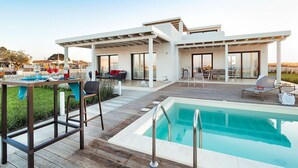 A modern outdoor pool area with a wooden deck, lounge chairs, and a dining setup. - Villa Orietta, garden and pool - My Rental Homes (Noto)