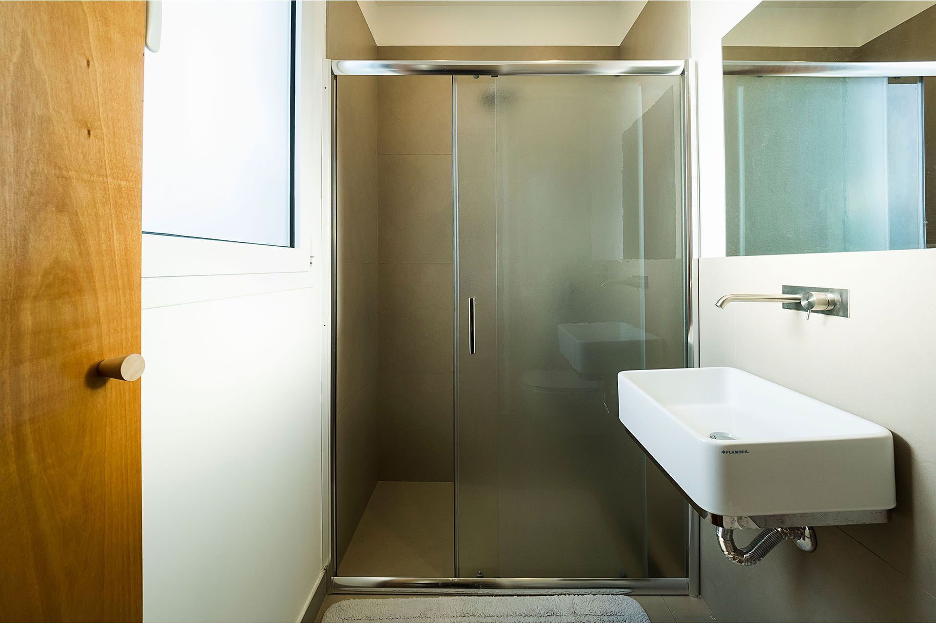 A bathroom with a glass shower door, a white sink, and a mirror above the sink.