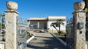 A gated entrance to a villa with a stone pathway leading to a white building with a tiled roof. - Villa Emma with private pool - My Rental Homes (Marsala)