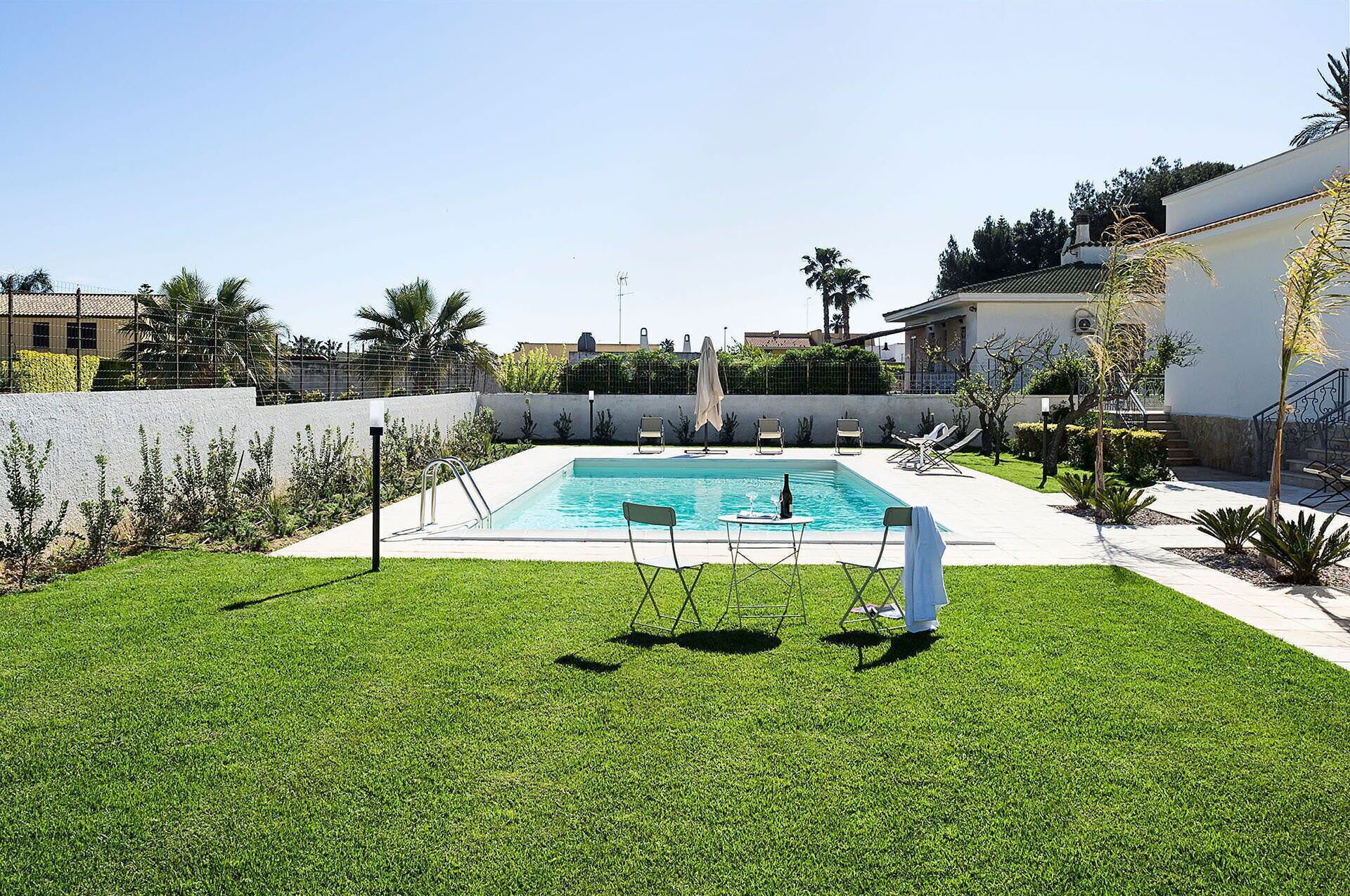 A rectangular swimming pool with a white deck, surrounded by a well-maintained lawn and various plants.