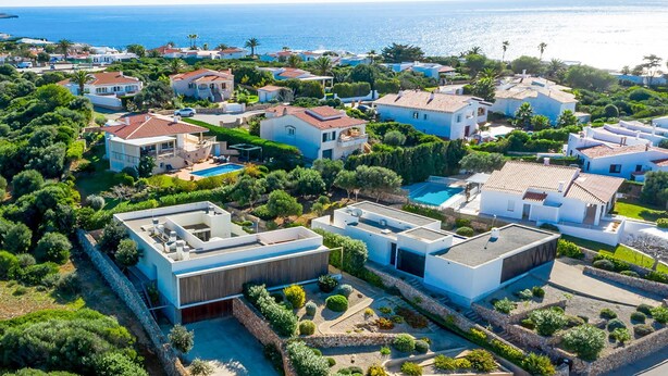 Vue aérienne d’un quartier résidentiel en bord de mer, avec des maisons modernes, une piscine et une végétation luxuriante.