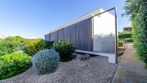 Un bâtiment moderne doté d’un toit en pente, entouré de gravier et de divers arbustes.