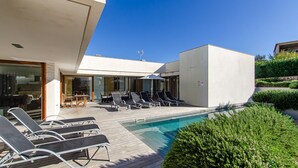 Un espace piscine extérieur moderne, doté de chaises longues et d’un coin repas.