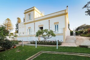 A two-story building with a balcony, a small garden area, and a staircase leading to the entrance. - The Flower Garden with pool - My Rental Homes (Marsala)