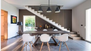 A modern kitchen with a dark wood table, white chairs, and a staircase with a black railing. - Sea Art Villa with private pool - My Rental Homes (Syracuse)