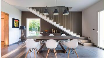 A modern kitchen with a dark wood table, white chairs, and a staircase with a black railing.
