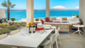 A terrace with a table set for dining, overlooking a body of water. - Sea Art Villa with private pool - My Rental Homes (Syracuse)