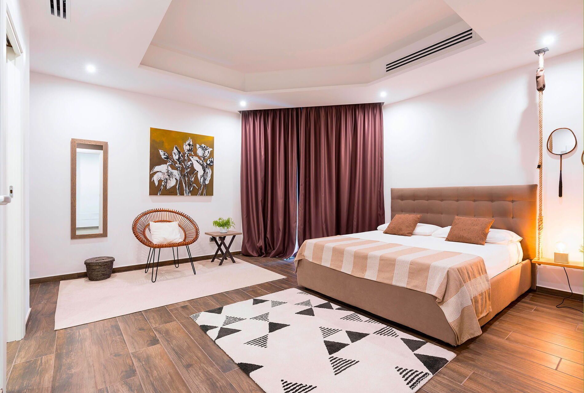 A modern bedroom with a large bed, a mirror, a painting, and a window with curtains.