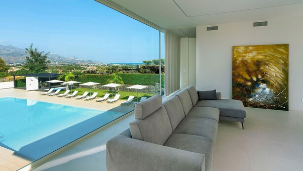 A modern living room with a large window overlooking a pool and a scenic landscape. - Villa Inga with private pool - My Rental Homes (Calatabiano)