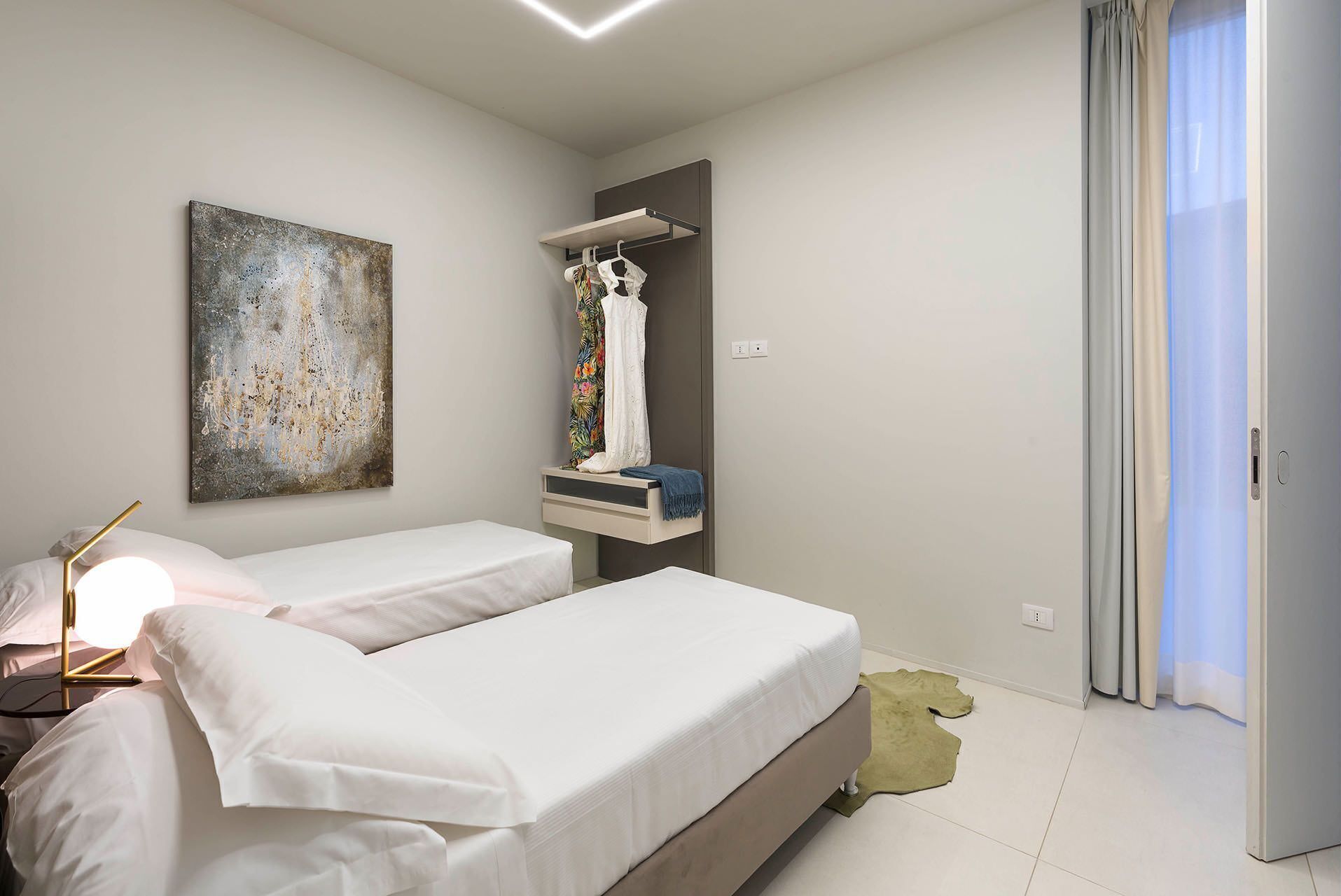 Une chambre d’hôtel moderne avec deux lits simples, une grande peinture abstraite, une armoire et une salle de bain avec un rideau de douche.