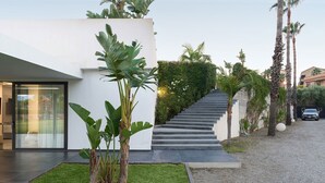 A modern house with a staircase leading to a second floor, surrounded by lush greenery and palm trees. - Villa Inga with private pool - My Rental Homes (Calatabiano)
