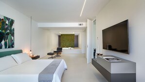 A modern hotel room with a large bed, a flat-screen TV, a minimalist bathroom, and a green wall feature. - Villa Inga with private pool - My Rental Homes (Calatabiano)
