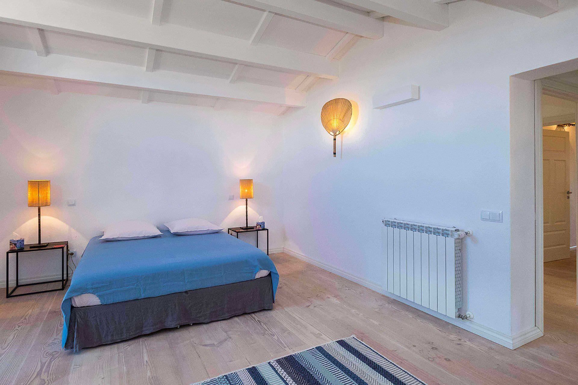A bedroom with a bed, two bedside lamps, a wall-mounted light fixture, and a radiator.