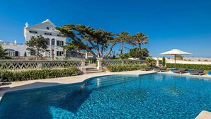 A clear blue pool with lounge chairs, a white building with arched windows, and a well-maintained garden. - My Rental Homes - Finca Design 10-min drive from Mahon with swimming pool (Mahon)
