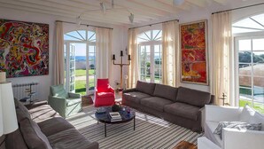 A spacious living room with a large window, a red chair, a grey sofa, and a coffee table. - My Rental Homes - Finca Design 10-min drive from Mahon with swimming pool (Mahon)