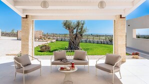 Un espacio de estar techado al aire libre con dos sillas y una mesa, con vistas a un jardín ajardinado y al mar.