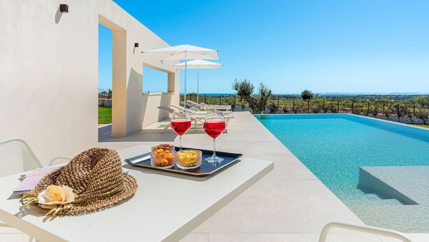 Zona junto a la piscina con vista al mar, una mesa con una bandeja de bocadillos y bebidas, y sillones de descanso.