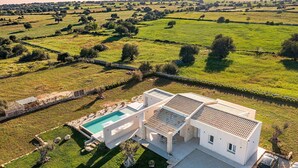 Una villa moderna con piscina, rodeada de amplios campos verdes y un muro de piedra.