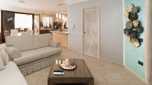 Ein Wohnzimmer mit einer Couch, einem Couchtisch mit Dekoration, einer Küchenzeile mit Spüle und Schränken sowie einer türkisblauen Akzentwand mit dekorativen Muscheln.