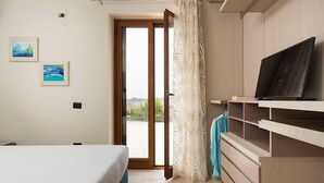 Ein Schlafzimmer mit einem Bett, einem Fernseher auf einem Holzboden, einer Tür zu einem Balkon und zwei gerahmten Bildern an der Wand.