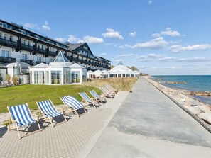Un hôtel situé en bord de mer, avec une rangée de chaises de plage, un patio couvert et une vue sur la mer.