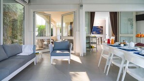 Een ruime woonkamer met een bank, stoelen, een ontbijtgedekte eettafel en grote ramen met uitzicht op het buiten.