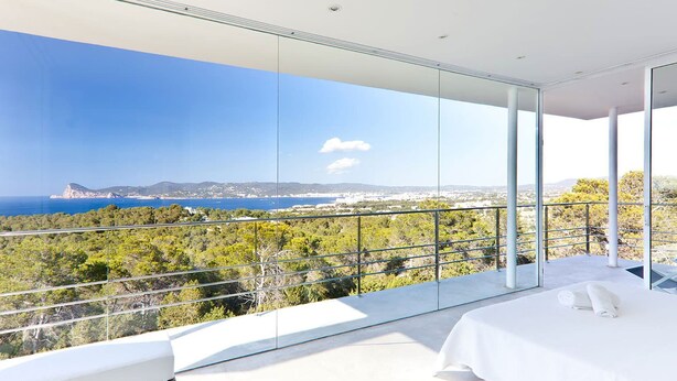 A modern bedroom with a large glass balcony overlooking a coastal landscape. - My Rental Homes - Villa Twilight with private pool and sea view (San Jose)