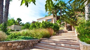 A stone staircase leading to a building with a stone wall on one side and a lush garden on the other.