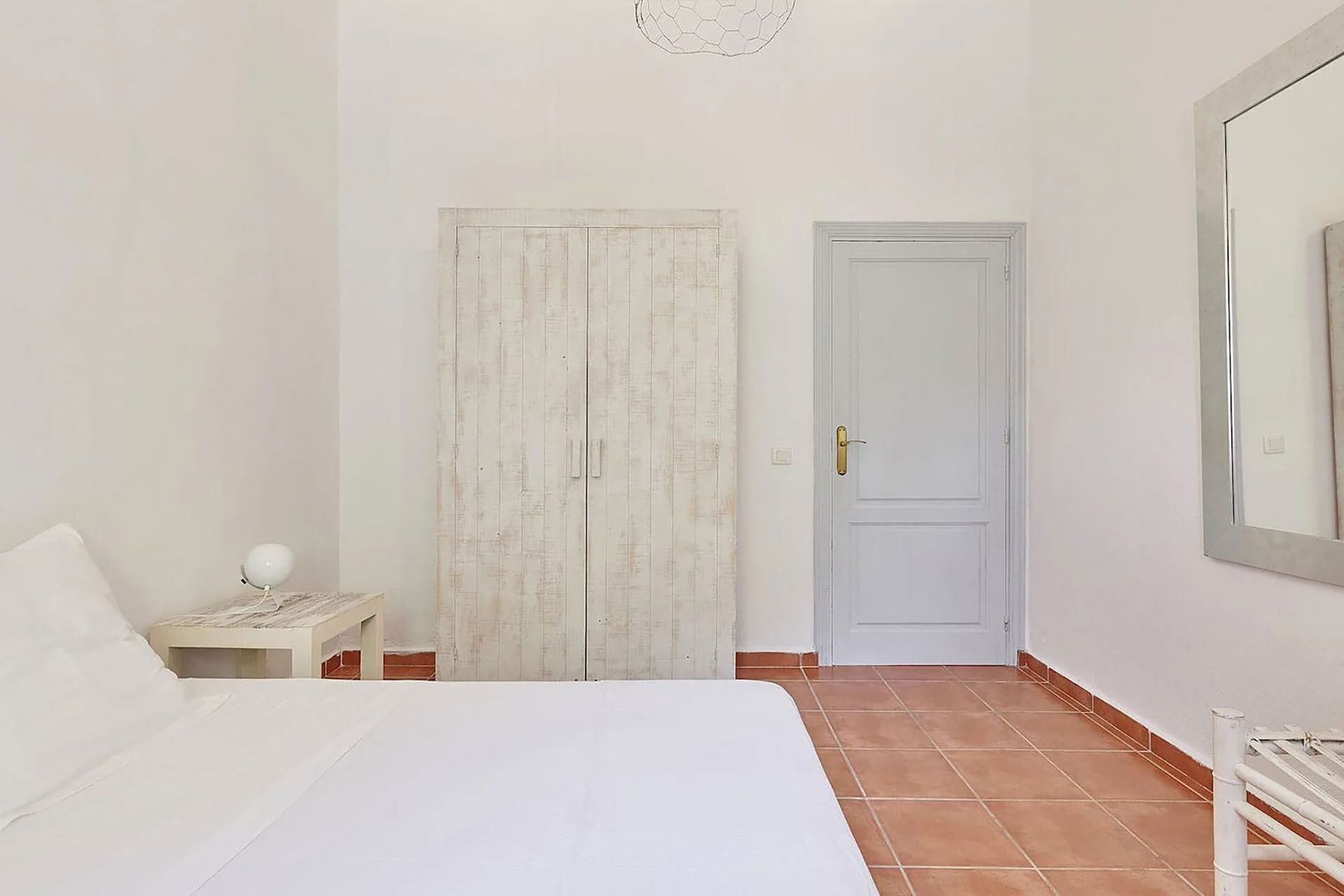 Un dormitorio con cama, mesita de noche, armario, puerta y radiador.