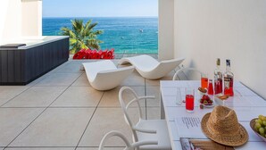 Ein Balkon mit Blick auf das Meer, weiße Liegestühle, ein Tisch mit Getränken und Snacks sowie ein rotes Schild.