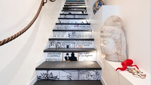 A staircase with black and white comic strip panels, a classical sculpture, and a red sculpture on the right side. - Casa Light Blu sea front home - My Rental Homes (Letojanni)