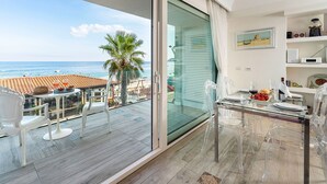 A balcony with a glass door, a dining table set with glasses and plates, and a view of the sea. - Casa Light Blu sea front home - My Rental Homes (Letojanni)