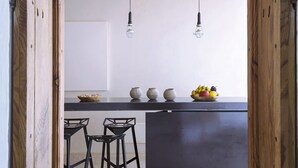 Une cuisine avec un plafond en bois, deux luminaires suspendus, un panier de fruits et trois pots en céramique posés sur le comptoir.