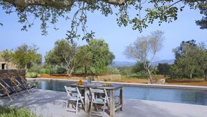 Un espace aménagé au bord de la piscine, avec une table et des chaises, entouré de verdure et délimité par un mur de pierres.