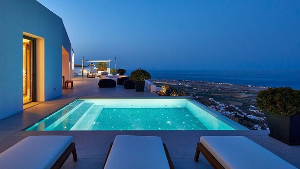 Ein moderner Poolbereich im Freien mit Blick auf das Meer, Liegestühlen und einer gut beleuchteten Terrasse.