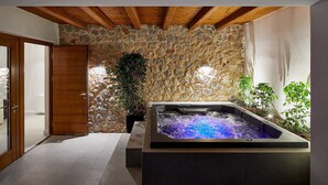 Ein Wellnessbereich mit Steinwand, Holzbalken, Whirlpool und Topfpflanzen.
