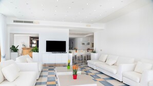 Ein modernes Wohnzimmer mit weißen Sofas, einem Flachbildfernseher und einem Schachbrettmuster-Boden.