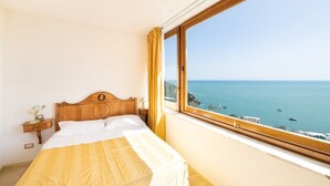 Ein Schlafzimmer mit einem hölzernen Bett, einem Nachttisch und einem großen Fenster mit Blick auf das Meer.