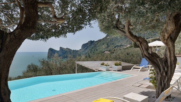 Ein Infinity-Pool mit Blick auf das Meer und die Berge, umgeben von Liegestühlen und einer Pergola.