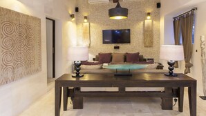 A modern living room with a dark wooden table, two side lamps, a sofa with cushions, a flat-screen TV mounted on a textured wall, and a decorative wall piece. - Villa in Santa Eulària Des Riu with 4 bedrooms sleeps 8 (Santa Eulària Des Riu)