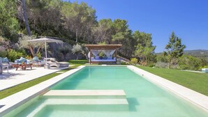 A rectangular swimming pool with a wooden deck and lounge chairs on one side, surrounded by greenery and trees. - Villa in Santa Eulària Des Riu with 4 bedrooms sleeps 8 (Santa Eulària Des Riu)