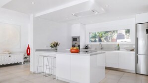 Een moderne keuken met witte kasten, een centraal eiland, een roestvrijstalen koelkast en een raam met uitzicht op groen.