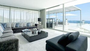 Un salon moderne avec un canapé, une table basse et une vue sur la mer grâce à de grandes fenêtres.